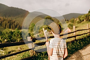 A boy walks along a dirt road in a village in the summer in the Alpine mountains.