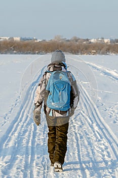 A boy walks along the road in winter with a backpack through a snowy wasteland. The concept of the road to school in the