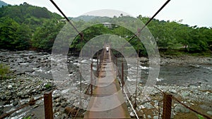 A boy walks along a suspension bridge over a mountain river.