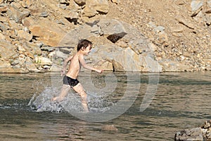 A boy walks quickly through the shallow water of a mountain river. He makes a lot of splashes