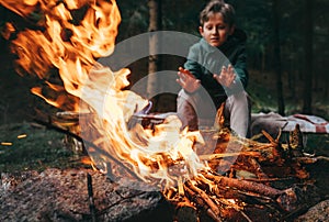 Boy warms hands near the campfire photo