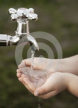 Boy washes his hand under the faucet in garden