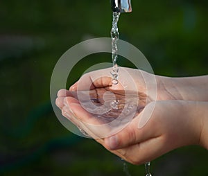 Boy washes his hand under the faucet in garden