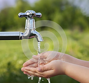 Boy washes his hand under the faucet in garden