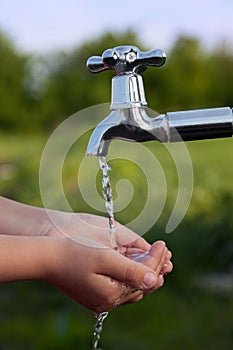 Boy washes his hand under the faucet in garden