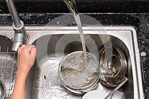 boy washing dishware in kitchen sink with soapy sponge