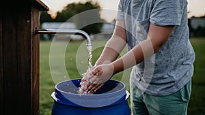 Boy washing his hands with water from a well. Well with a pump for outdoor washing in garden.