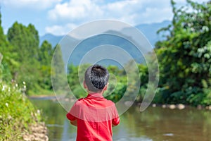 The boy watched the stream flow from the mountains, The background mountains and trees.