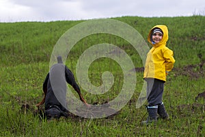 A boy watches as a Doberman dog digs its paws and tears pieces of earth with its teeth in search of a rodent or gopher