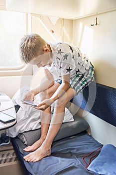 Boy watches film using smartphone sitting on bed backrest