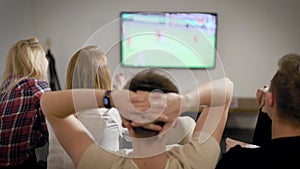 Boy watching football match on tv with girls, friends spending time together indoor.