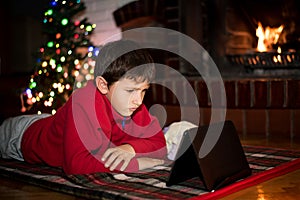 Boy watching tablet beside Christmas tree a