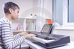 Boy watching video lesson at digital tablet computer and playing piano at home. Online learning remote education