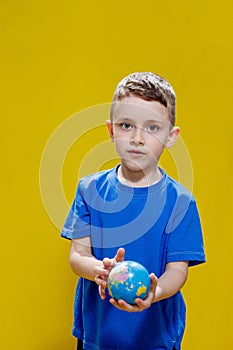 A boy wearing a blue t-shirt, holding a globe of the Earth in his hands, isolated on a simple yellow background, studio portrait
