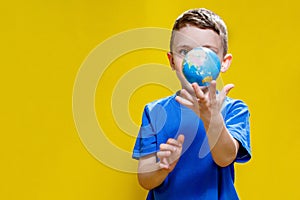 A boy wearing a blue t-shirt, holding a globe of the Earth in his hands, isolated on a simple yellow background, studio portrait