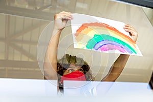 Boy wearing face mask sticking rainbow painting to the window