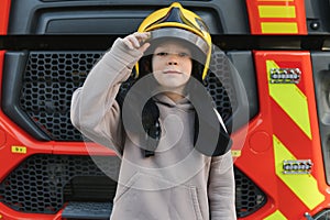 A boy wearing a fireman's helmet near a fire truck.