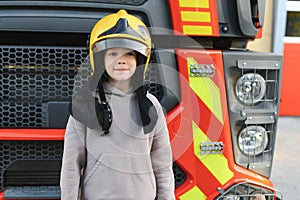 A boy wearing a fireman's helmet near a fire truck.