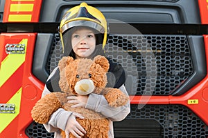 A boy wearing a fireman& x27;s helmet near a fire truck.