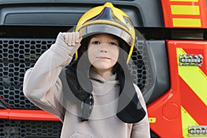 A boy wearing a fireman& x27;s helmet near a fire truck.