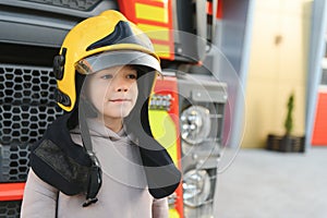 A boy wearing a fireman& x27;s helmet near a fire truck.