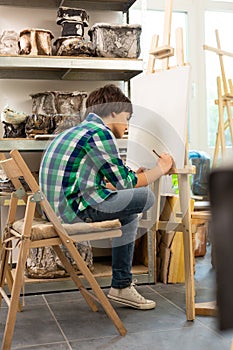 Boy wearing jeans feeling busy while drawing in art school