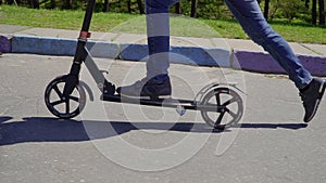 Boy wearing jeans and sneakers riding on kick scooter on the road