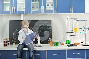 Boy wearing lab coat making notes in clipboard in science laboratory