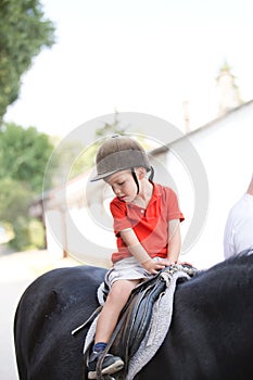 A boy wearing orange shirt and a helmet sitting on top of a horse