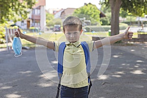 Boy wearing a protective mask with a backpack behind his back in the schoolyard on the first school day after isolation or