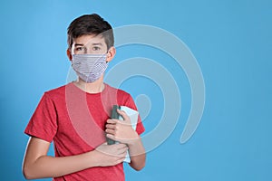 Boy wearing protective mask with books on light blue background, space for text. Child safety