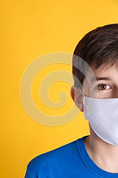 Boy wearing protective mask on yellow background, closeup. Child safety