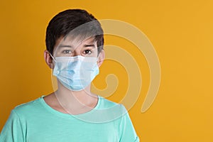 Boy wearing protective mask on yellow background, space for text. Child safety