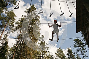 boy wearing a safety harness and a helmet walking in a rope park