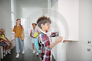 Boy wearing squared shirt opening locker while taking books