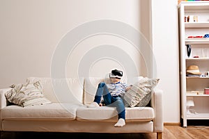 Boy wearing virtual reality goggles. Studio shot, white couch