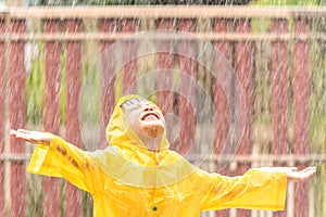 A boy wearing a yellow raincoat. Happy asian little child having fun to playing with the rain drops
