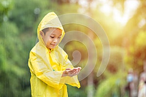 A boy wearing a yellow raincoat in public park. Happy asian little child having fun to playing with the rain drops. A boy enjoying