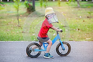 The boy wears a hat to prevent germs while he learns to ride a bike.