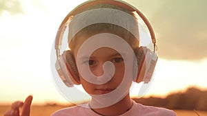 The boy wears headphones in a field at sunset