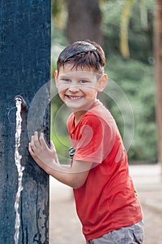 Boy with wet T-shirt. Playing with water. Water tap in the park.