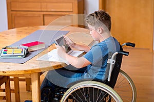 Boy in wheelchair doing homework and using tablet pc