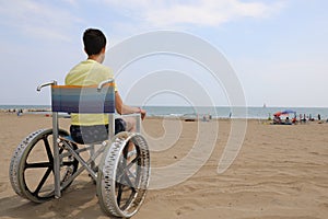 Boy in a wheelchair with metal wheels to move on the beach by th