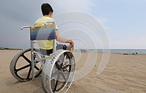 Boy in the wheelchair on the sandy beach by the sea and the spec