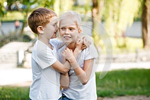 The boy whispers a secret in the girl's ear. Children for a walk in the park.