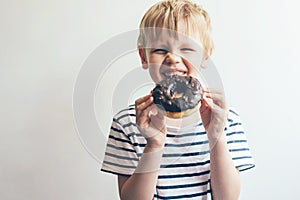 Boy on a white background holds a chocolate donut and laughs