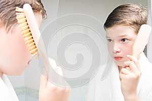 Boy, in a white bathrobe, in the bathroom, combing his hair, near the mirror