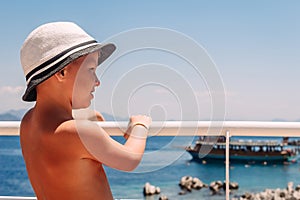 A boy in a white hat holding the railing on the ship and looking at the sea