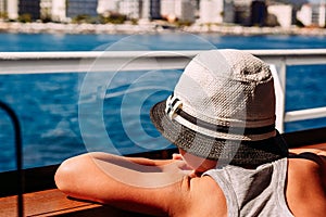 A boy in a white hat looking at the sea through the window of the ship