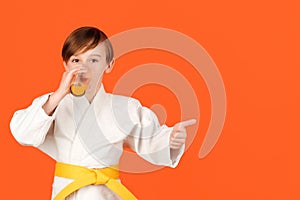 Boy in white kimono drinks water. Kid practicing karate on color background. Kid sport concept